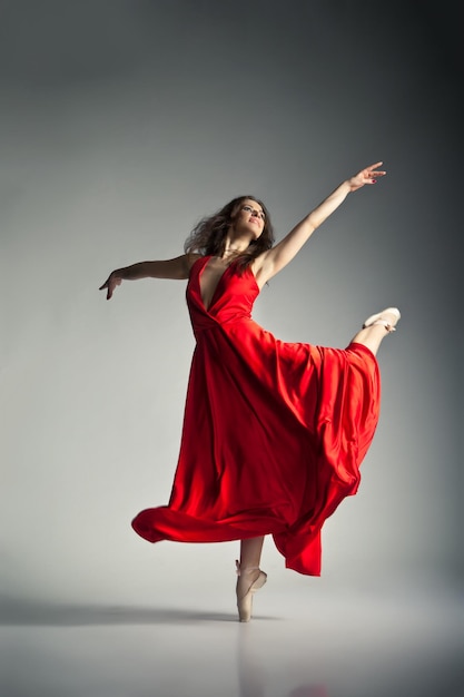 Foto splendida giovane ballerina che indossa un abito rosso su sfondo grigio scuro