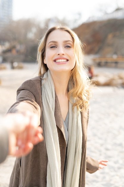 Splendida giovane donna bionda che tiene una mano con un sorriso e lo segue su una spiaggia