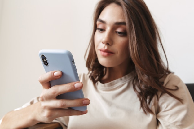 gorgeous young woman holding smartphone and sitting on sofa in apartment