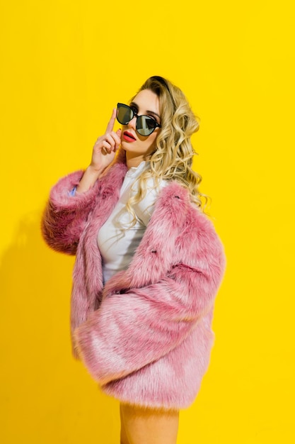 Gorgeous young woman posing in luxurious fur coat and bodysuit. Fashion, beauty. Studio shot.