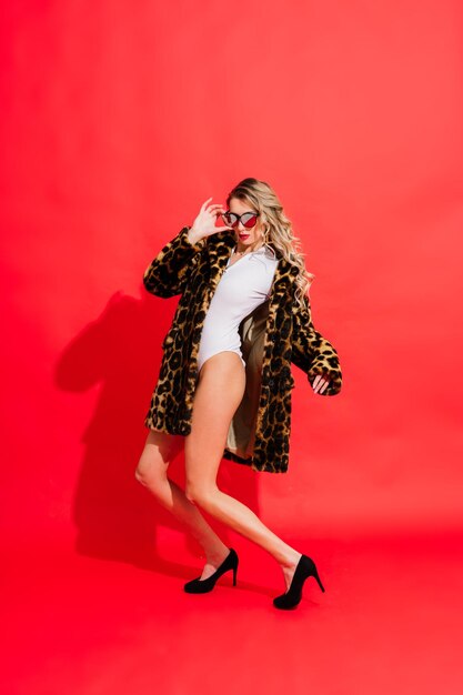 Gorgeous young woman posing in luxurious fur coat and bodysuit. Fashion, beauty. Studio shot.