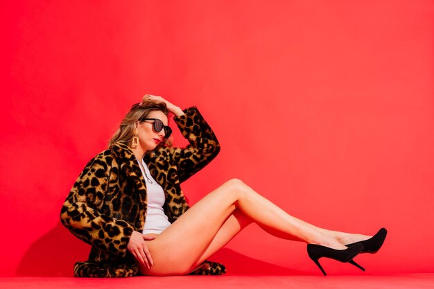 Gorgeous young woman posing in luxurious fur coat and bodysuit. Fashion, beauty. Studio shot.