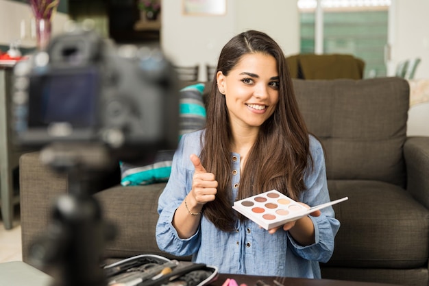 Gorgeous young woman reviewing and endorsing cosmetic products for her beauty video blog at home