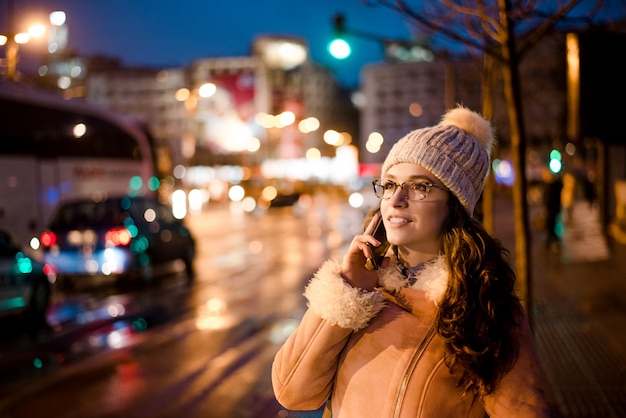 Gorgeous young woman talking on phone in city street, traffic lights on background.