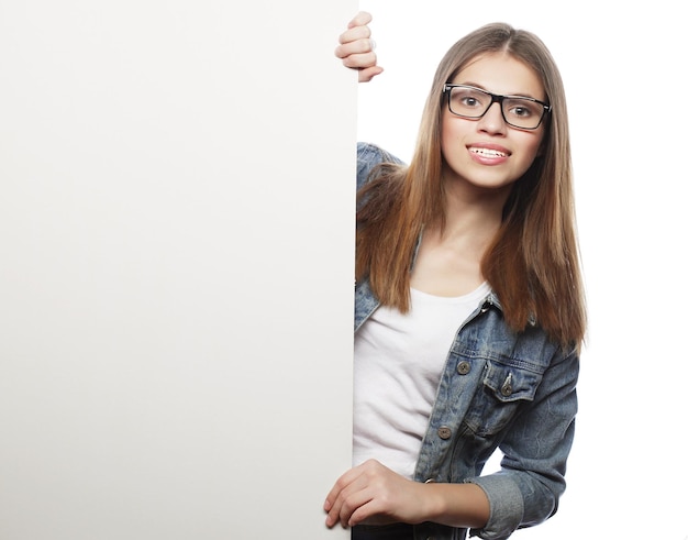 Gorgeous young woman wearing glasses pointing at a board while standing against a white background