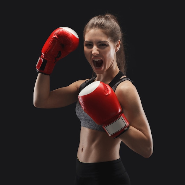 ボクシンググローブを持ったゴージャスな若い女性、防御位置に立って、戦う準備ができて、スペースをコピーします。黒の背景、ローキーでスタジオ撮影。キックボクシングとファイトスポーツのコンセプト