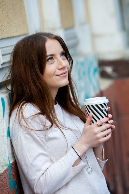 街の通りでコーヒーを飲みながらゴージャスな若い女性