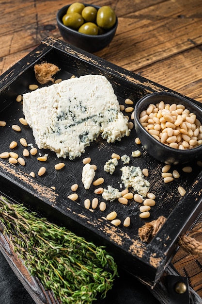 Gorgonzola cheese in a wooden tray with olives and nuts. Wooden background. Top view.