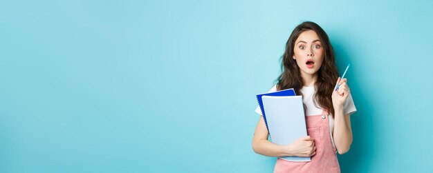 Photo got an idea excited young woman student holding notebooks and pen raising hand while having a plan t