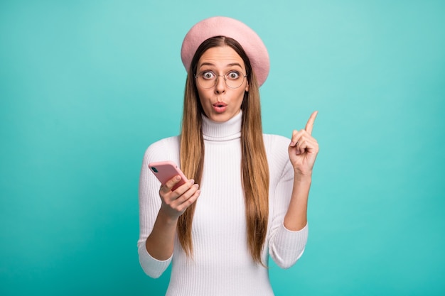 Got it! Photo of beautiful shocked lady hold telephone clever person have smart idea raise index finger open mouth wear specs pink beret cap white turtleneck isolated teal color background