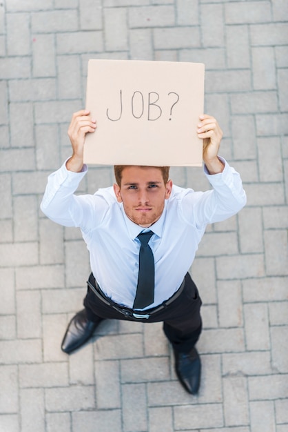 Hai un lavoro? vista dall'alto di un bel giovane in camicia e cravatta che mostra poster con messaggio di testo di lavoro mentre si trova all'aperto