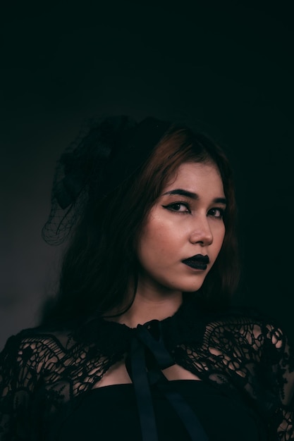 A gothic Indonesian woman wearing a beautiful black hat while dressing like a witch in black