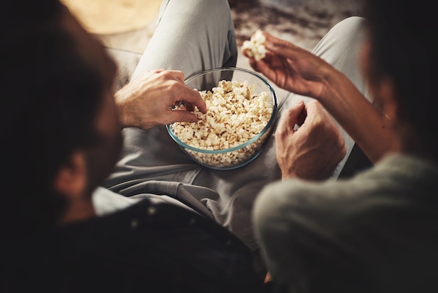 私がポップコーンを共有しているなら、愛しなきゃいけない。自宅で一緒にポップコーンを食べながらソファに座っている若いカップルのリアビューショット