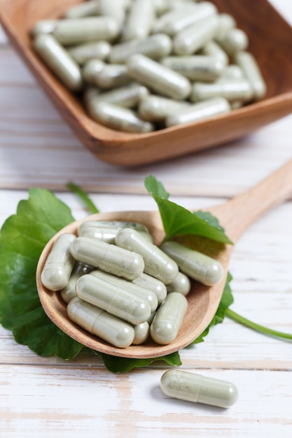 Photo gotu kola capsule in wooden spoon. asiatic pennywort.