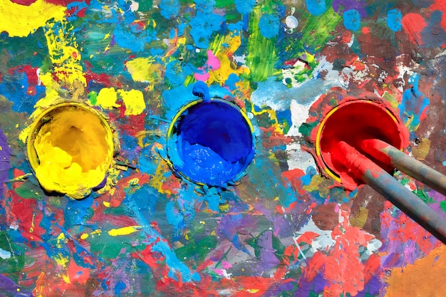 Gouache paint table with paint smears and cups with yellow, blue and red paints