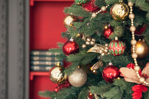 Goud en rood Kerstmisspeelgoed, ballen, slingers op een vuren tak op donkerrode achtergrond.