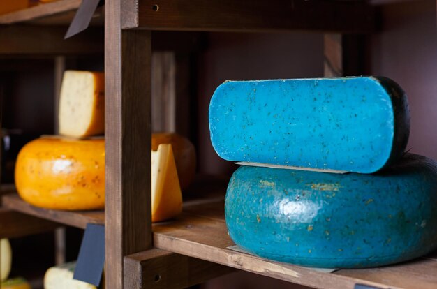 Gouda pesto blue cheese as wheel and piece on grocery shop wooden shelf, closeup