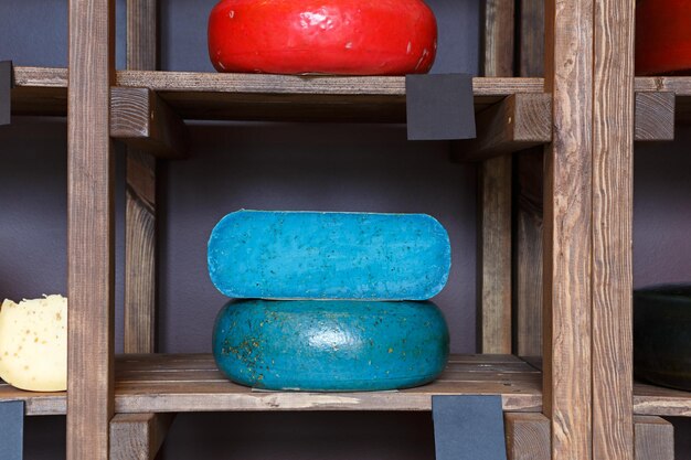 Gouda pesto blue pesto cheese as wheel and piece on grocery shop wooden shelf, closeup