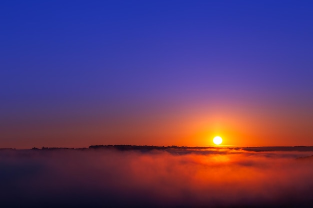 Goudblauwe zomerzonsopgang boven mist zonder wolken in minimalistische compositie