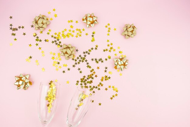 Foto gouden bogen en confetti sterren met glazen liggen op een roze achtergrond kopie ruimte