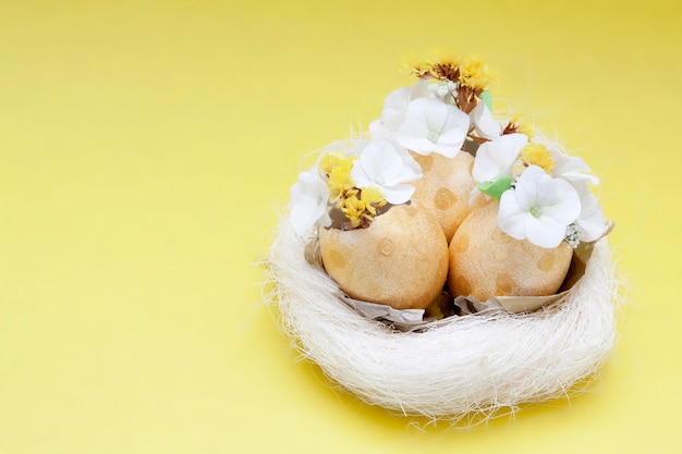 Gouden eieren met bloemen in een nest op gele ondergrond