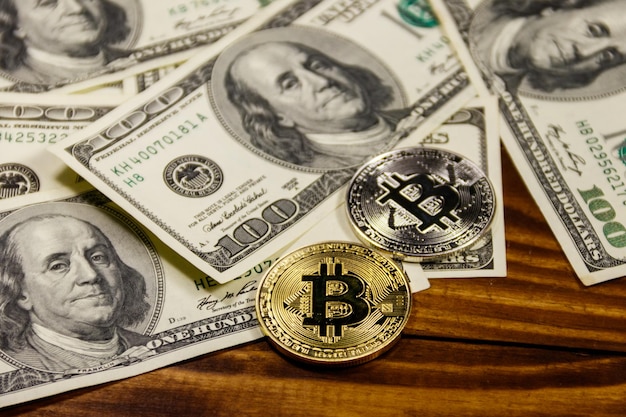 Gouden en zilveren bitcoins en honderd-dollarbiljetten op houten bureau