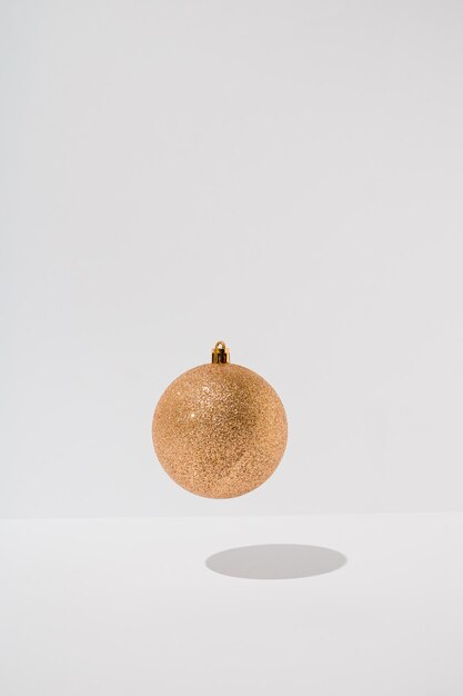 Gouden glanzende kerstbal die boven een witte achtergrond zweeft Minimale vakantiegroet concept