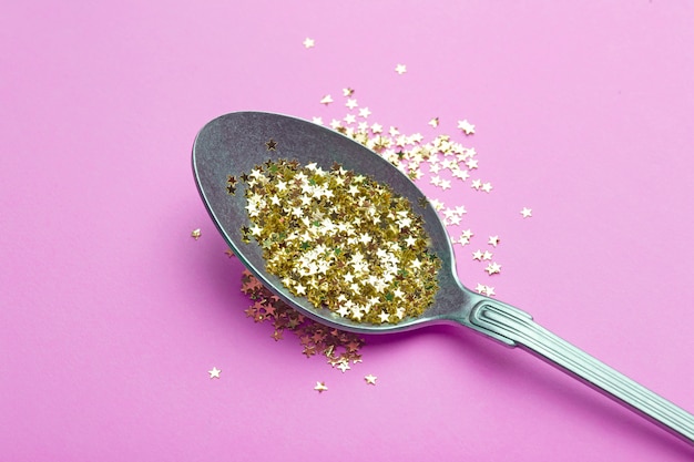 Gouden glitter in een lepel op roze oppervlak