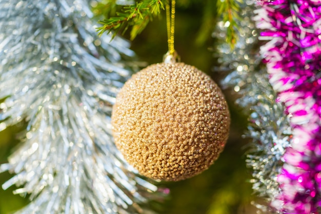 Gouden kerstbal en glanzend klatergoud hangend aan de tak van de boom. Vergrote weergave van Xmas vakantie decoratie, concept voor Happy New Year. Selectieve focus op de voorgrond, wazig bokeh op de achtergrond.