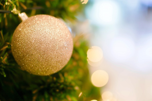Gouden Kerstmisbal die op Pijnboomboom op Kerstmisdag wordt verfraaid met onscherpe achtergrond