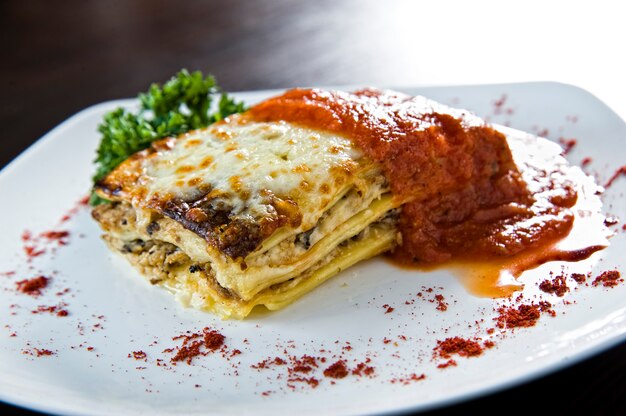 Gouden lasagne met vlees, tomaten, kaassaus en pasta in afwisselende lagen op een houten bord gegarneerd met basilicum