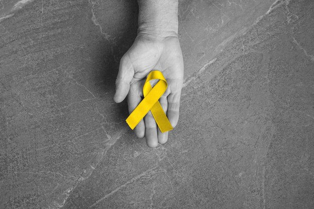 Gouden lint jeugdsymbool van de strijd tegen kanker bij kinderen in handen op grijze muur. concept van het helpen van patiënten met sarcoom en blaaskanker.