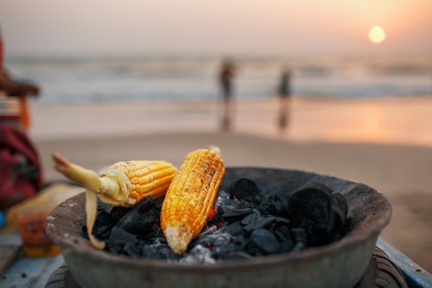 Gouden maïskolven op de kolen in de grill. Op het strand van Arambol bij zonsondergang. Aziatisch, Indiaas straatvoedsel