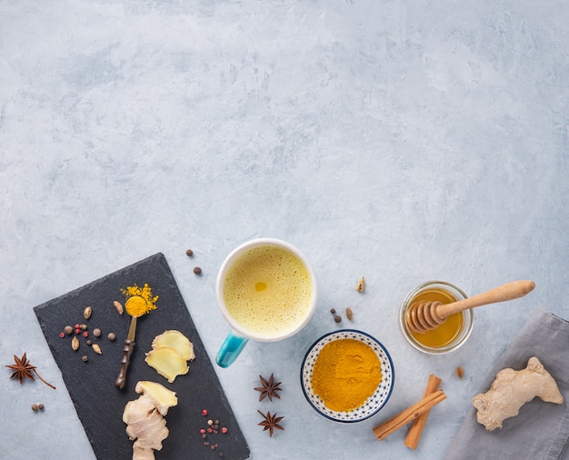 Gouden melk met kurkuma, kruiden en honing op een grijze achtergrond