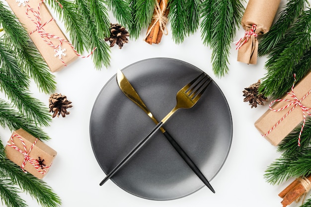 Gouden mes en vork gekruist op zwarte plaat op kersttafel met frame van dennentakken met...