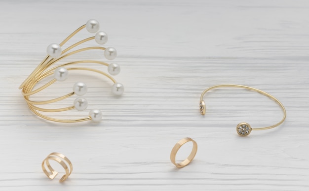 Gouden parel en gouden diamanten armbanden en ringen op witte houten oppervlak