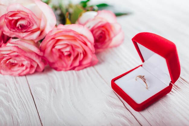 Gouden ring met edelstenen in rode geschenkdoos en boeket rozen