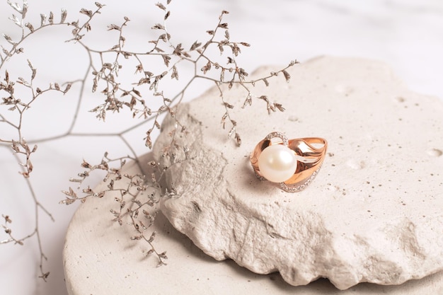 Gouden ring met parel op stenen podium met droogbloemen