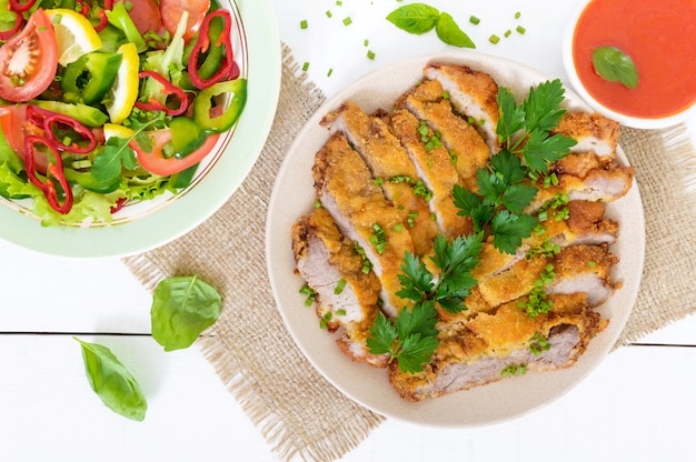 Gouden schnitzel gehakte plakjes en een kom groente salade op een witte houten tafel. Bovenaanzicht. Gezond dieet.