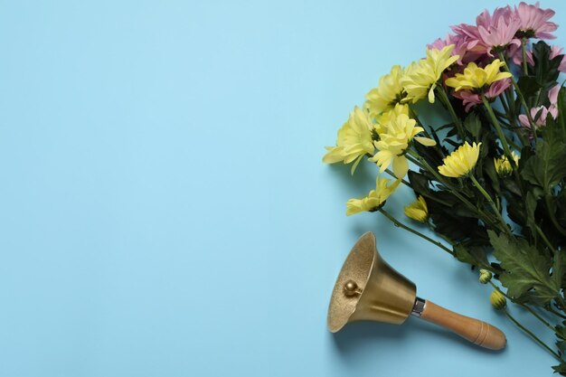 Gouden schoolbel en boeket van prachtige chrysantenbloemen op lichtblauwe achtergrond plat leggen Ruimte voor tekst