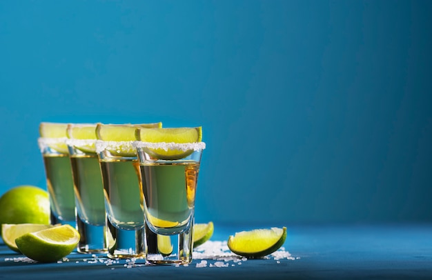 Gouden tequila met zout en limoenen in schoten staat op blauw