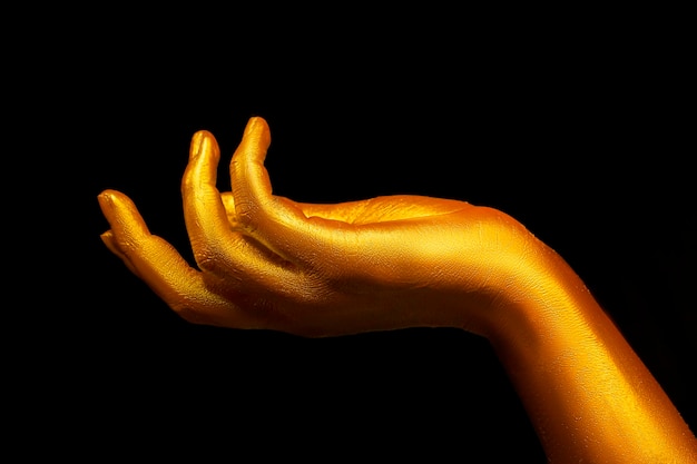 Gouden vrouwelijke hand op een zwarte achtergrond Mooie vingers bedekt met goud