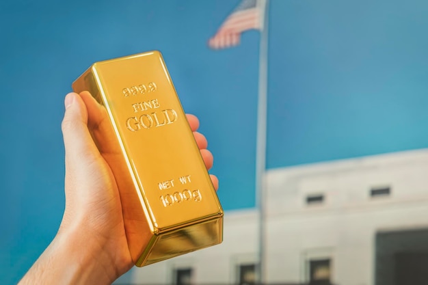 Goudstaaf in de hand van een man tegen de achtergrond van de gouden kluis van Amerika