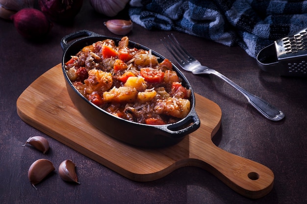Foto gulasch su un tagliere da cucina, cipolla rossa, aglio, tovagliolo di stoffa e un pezzo di forchetta.