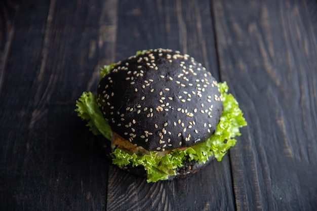 Hamburger nero gourmet con salsa piccante su tavola di legno e sfondo nero. focalizzazione morbida. messa a fuoco selettiva