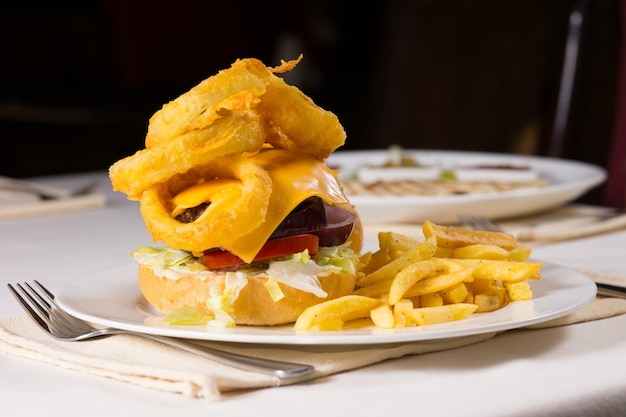 Изысканный чизбургер и картофель фри на тарелке в сервировке на столике в ресторане