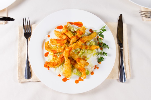 Piatto di carne fritta croccante gourmet sul piatto rotondo bianco, cenare sul tavolo bianco con utensili.