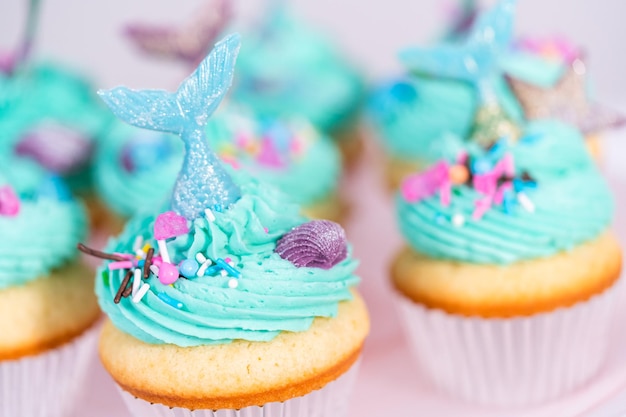 Gourmet mermaid cupcakes topped with blue buttercream frosting and decorated with sprinkles and chocolate mermaid tails.