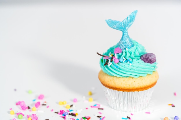 Cupcakes gourmet a forma di sirena conditi con glassa di crema al burro blu e decorati con confettini e code di sirena al cioccolato.