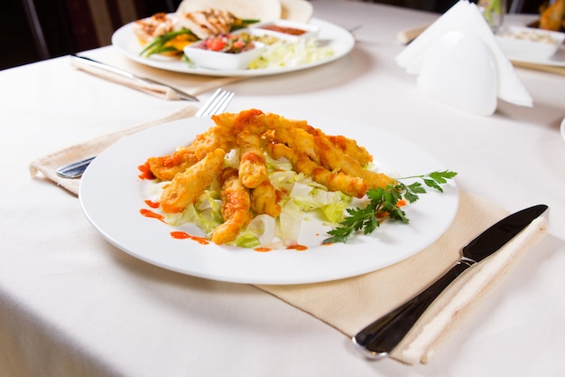 Gourmet gustoso fritto di carne di pesce con erbe e verdure su piatto rotondo bianco servito sul tavolo.